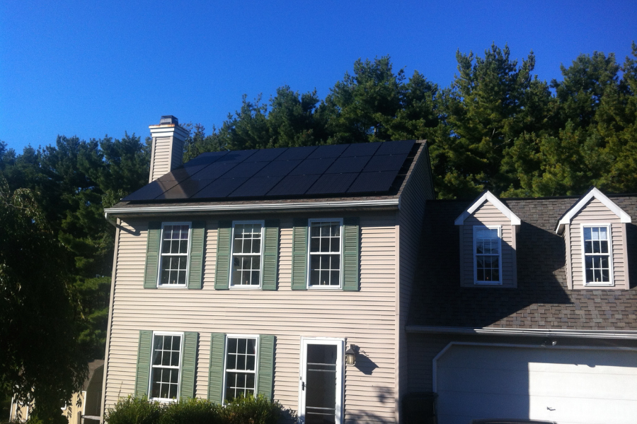 all black solar panels on roof of home with tan siding and green shutters