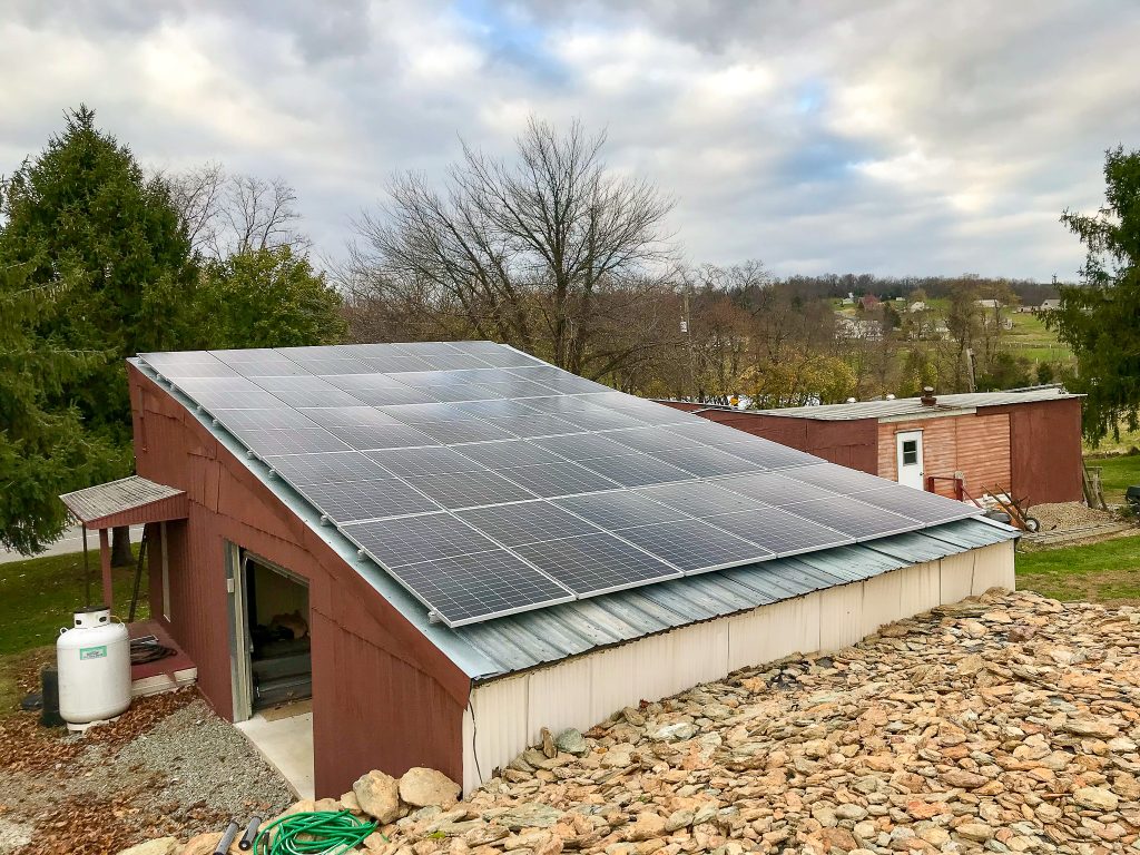 Large brown metal shed with roof full of neatly installed solar panels - Various trees and farmland visible in the distance - Rooftop solar panel installation by Belmont Solar - A trusted Solar Installer in Manheim PA